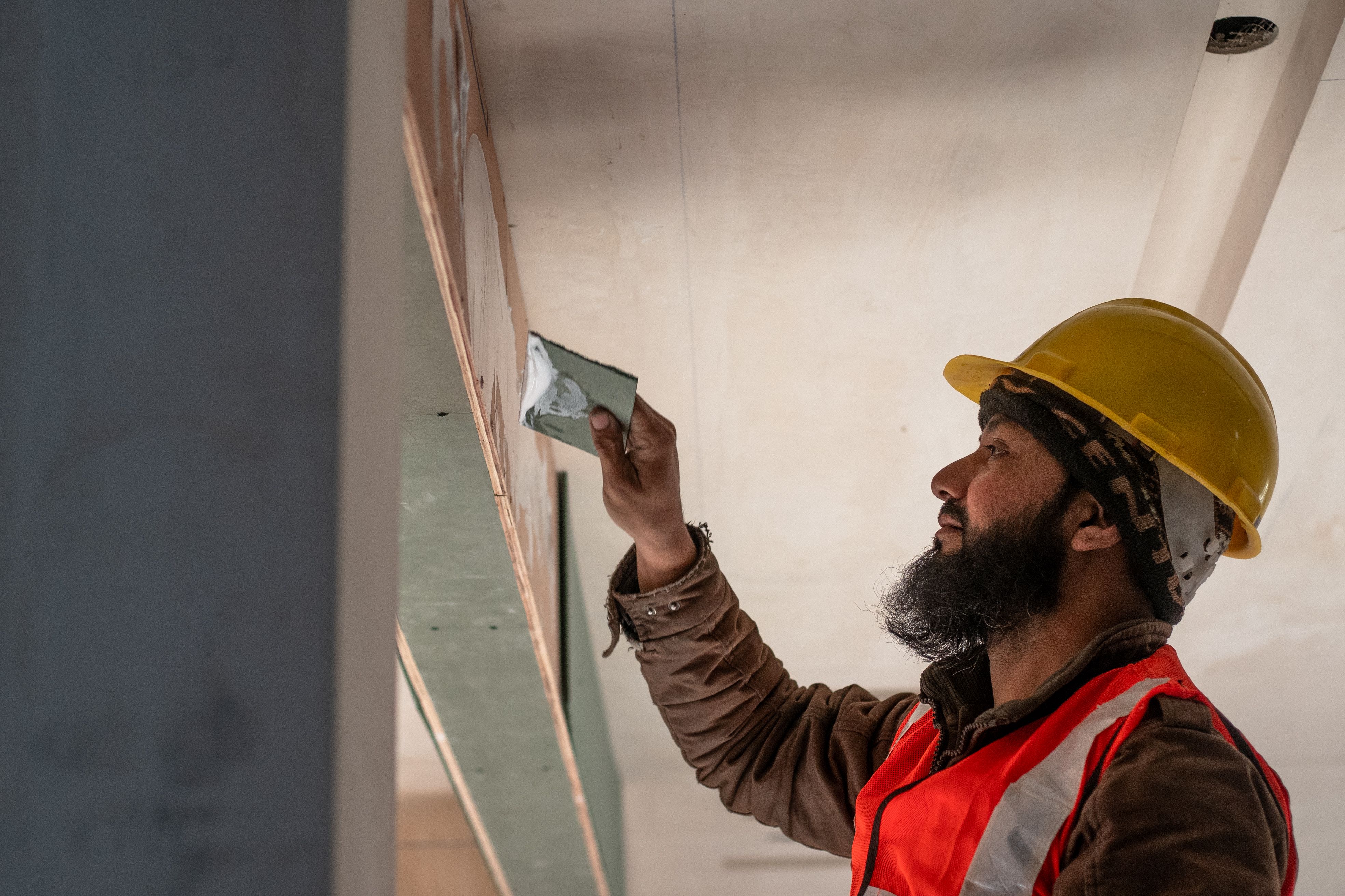 Self-employed plasterer smoothing a wall, highlighting the physical demands of tradesman work